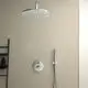 Runder Duschkopf in Chromfarbe, montiert an der Decke, mit einer Handbrause und einem Steuerthermostat an der Wand. Ideal Standard Design in minimalistischer Badezimmerumgebung.